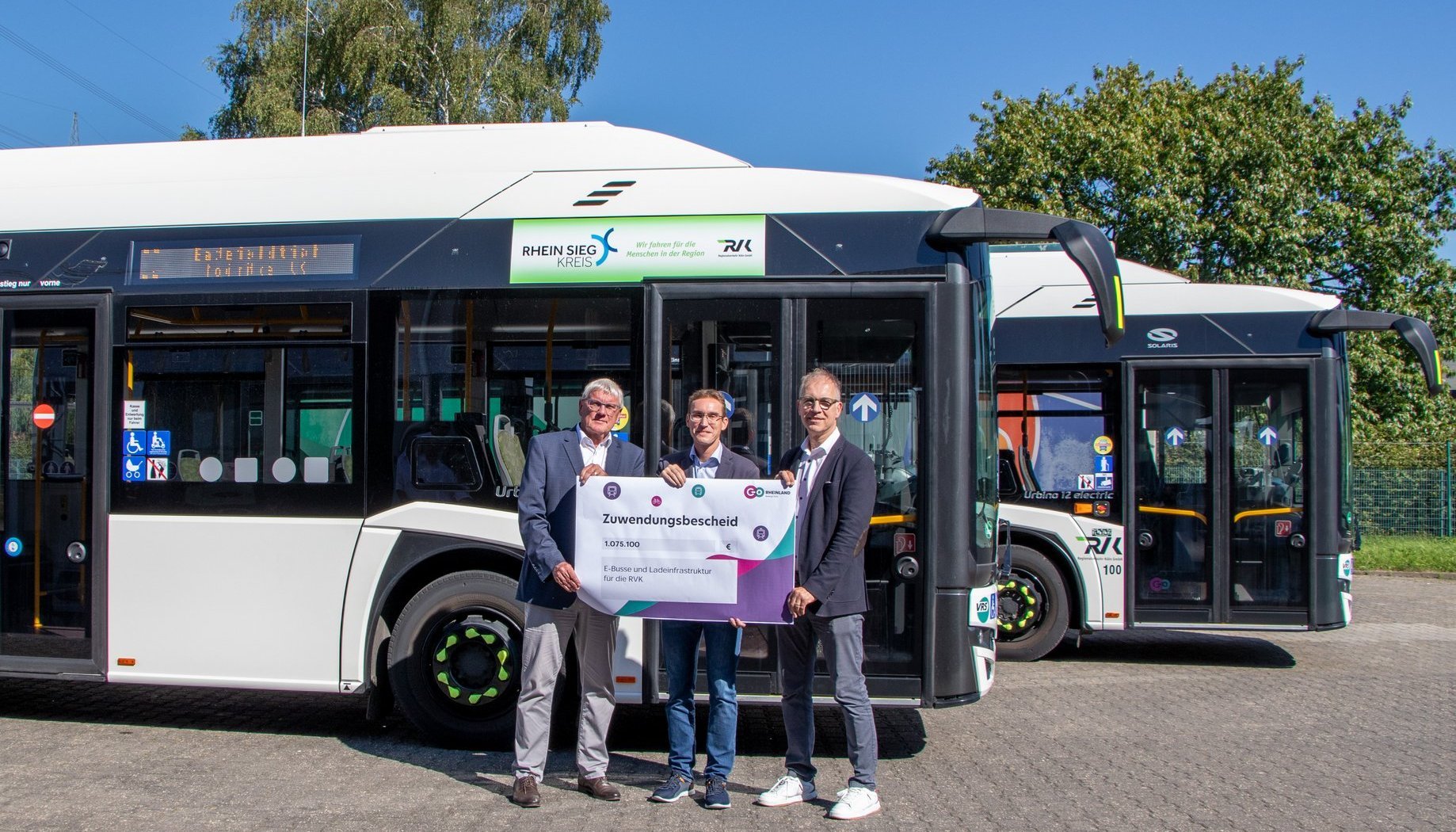 Drei Personen halten ein Schild mit einem Zuwendungsbescheid über 1.075.100€