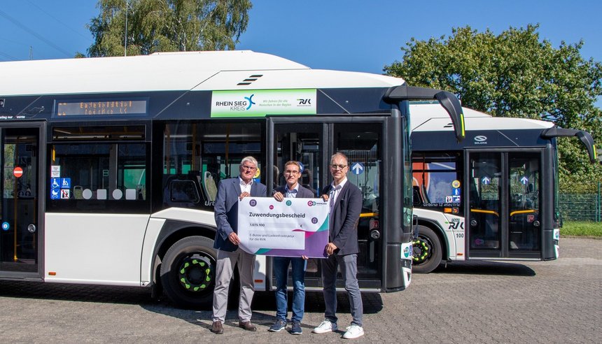 Drei Personen halten ein Schild mit einem Zuwendungsbescheid über 1.075.100€