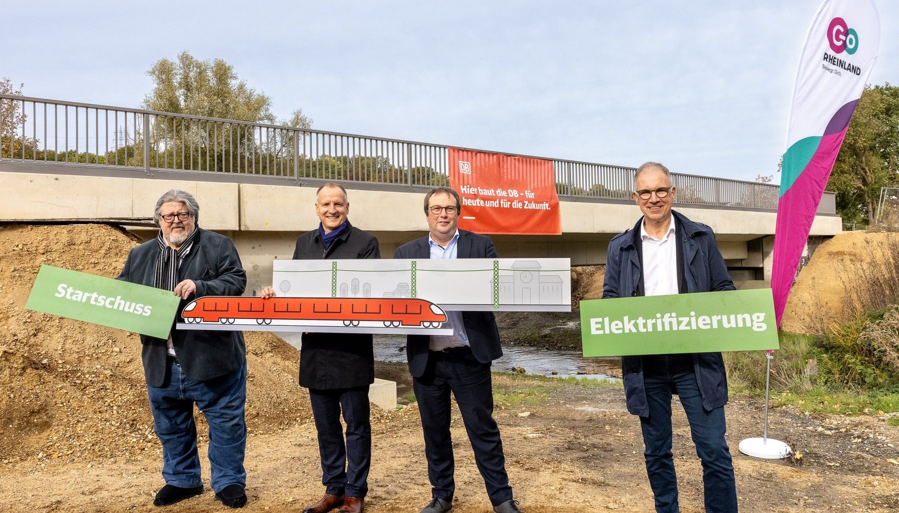 Vier Personen stehen vor einer Baustelle an einer Eisenbahnbrücke