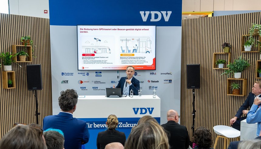 Das Bild zeigt Eduard Rollmann, Leiter des Kompetenzcenter Marketing NRW, der das Projekt "D-Data" einem interessierten Publikum auf der Innotrans in Berlin vorstellt. © VDV / Michael Fahrig