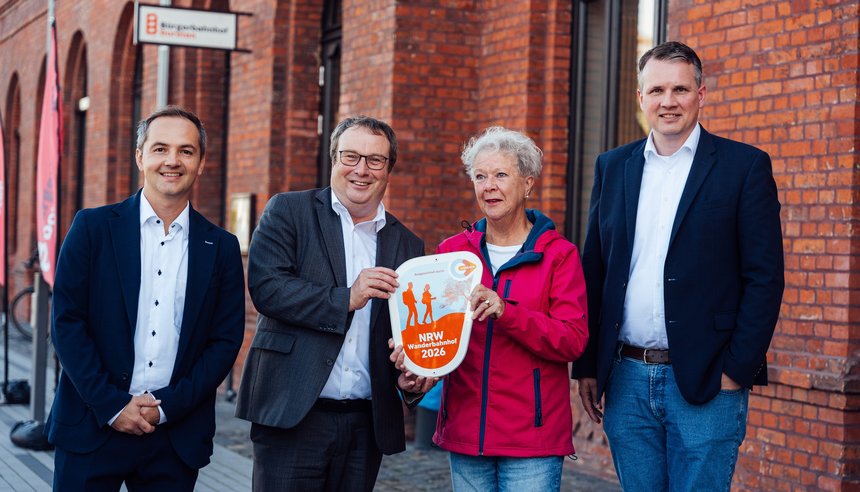 Die offizielle Plakette für den NRW-​Wanderbahnhof 2026 wird von Oliver Krischer, Minister für Umwelt, Naturschutz und Verkehr NRW (2. v. l.), übergeben.