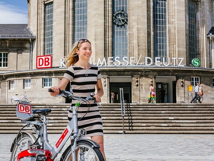 Junge Frau mit DB-Leihrad vor Bahnhof Köln Messe/Deutz