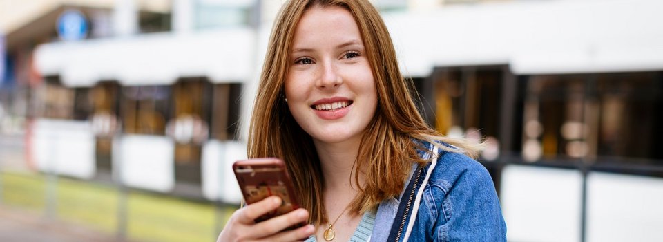 Junge Frau mit Handy vor Stadtbahn