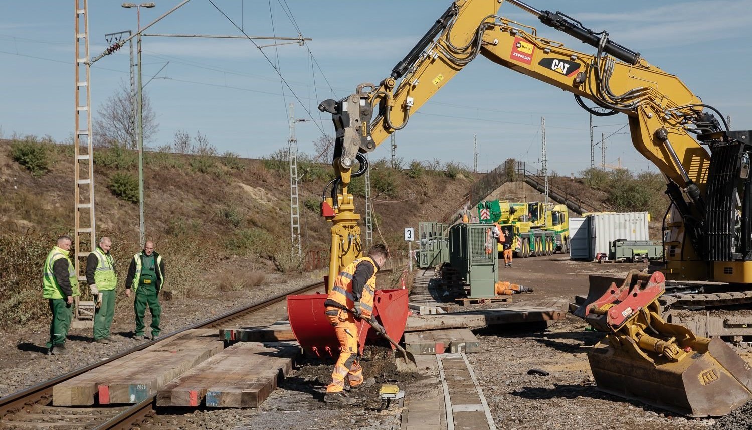 Bauarbeiter und ein Bagger arbeiten an Gleisen