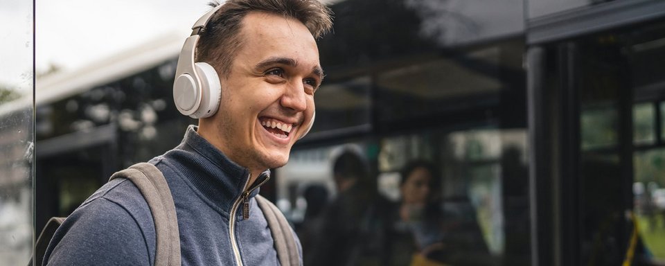 Junger Mann mit Kopfhörer und Handy beim Einsteigen in den Bus Junger Mann mit Kopfhörer und Handy beim Einsteigen in den Bus