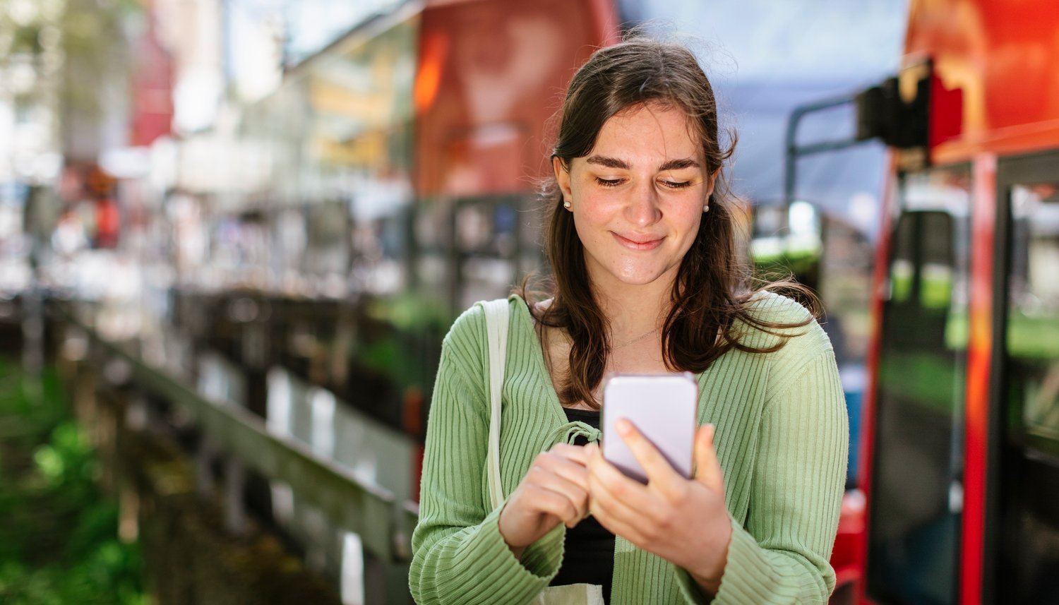 Junge Frau mit Handy an Stadtbahn-Haltestelle