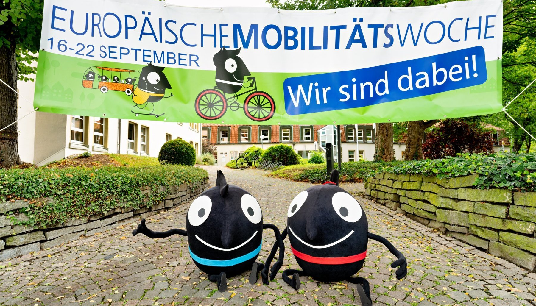 Die Maskottchen der Aktion stehen vor einem Banner mit der Aufschrift "Europäische Mobilitätswoche"