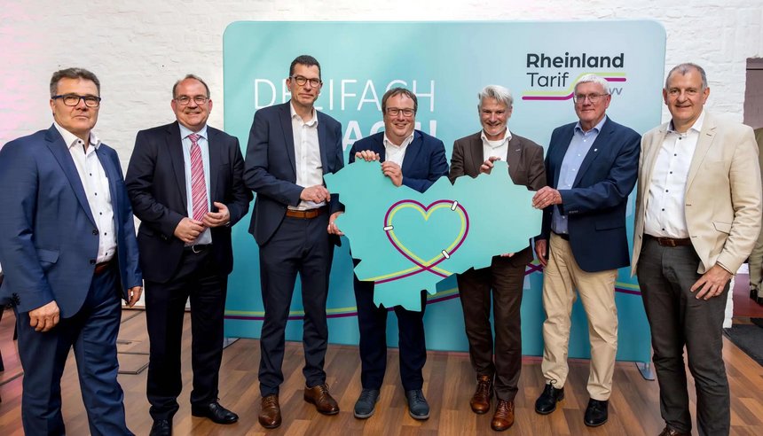 Das Bild zeigt v.l.: Volker Otto, Dr. Ralf Nolten, Hans-Peter Geulen, Minister Oliver Krischer, Michael Vogel, Sebastian Schuster und Joachim Adler mit einer Karte, die die Umrisse des neuen gemeinschaftlichen Tarifgebiets zeigt.